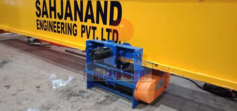 Blue wire rope hoist trolley beside a Sahjanand Engineering crane girder in the workshop